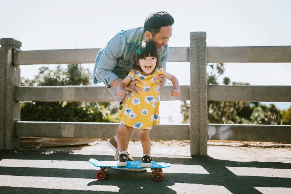 A dad teaching his daughter how to skateboard