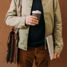 A man holds a cup of coffee in one hand and a laptop in the other, ready for the work day